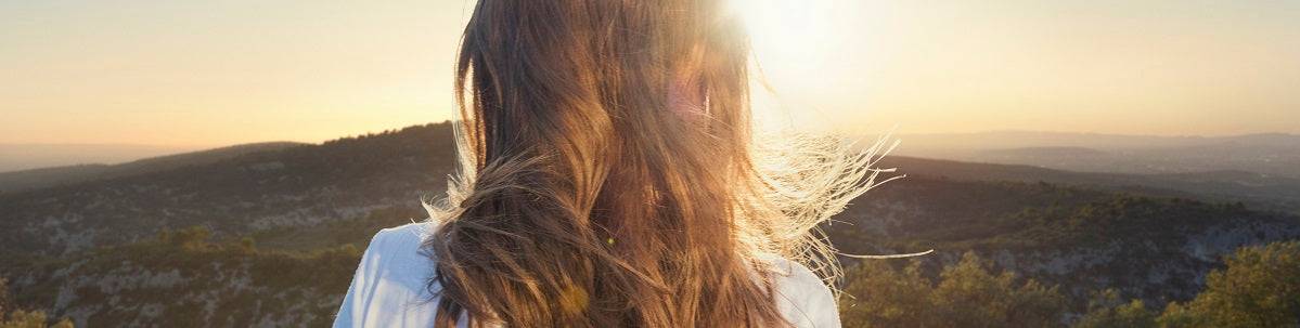 Cabello largo y brillante al atardecer; cuidado capilar L’Occitane con aceites esenciales para fortalecer y suavizar.